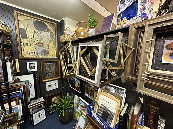 Picture of artwork on the wall, surrounding by empty frames, a plant, and wicker baskets.